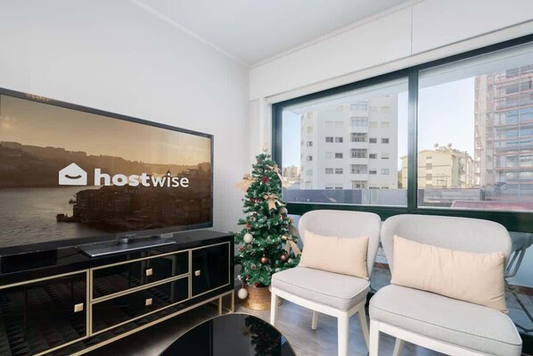 Una sala de estar moderna con un televisor grande que muestra 'hostwise', un árbol de Navidad y dos sillones blancos.