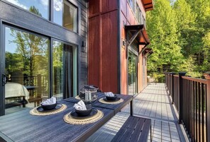 A deck with a long table set for dining, overlooking a forested area.