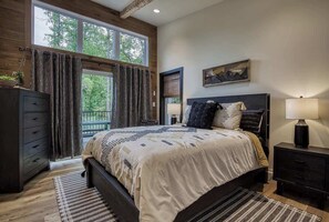 A bedroom with a large bed, a dresser, a nightstand, and a window with curtains.