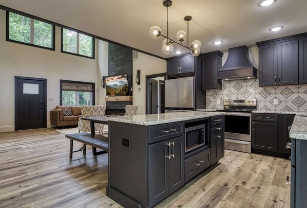 A modern kitchen with dark cabinetry, a large island, and a dining area with a bench.