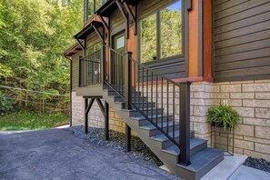 A two-story house with a wooden exterior and a stone foundation. There is a staircase with black railings leading to the upper floor.
