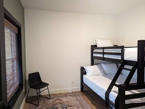Une petite pièce simple, avec un lit superposé, une chaise et une fenêtre équipée de stores.