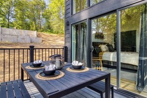 An outdoor deck with a table set for dining, surrounded by a wooden deck and a glass door leading to a bedroom.