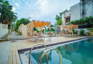 Ein Poolbereich mit zwei Liegestühlen unter Sonnenschirmen, einer gefliesten Terrasse und einem klaren Pool.