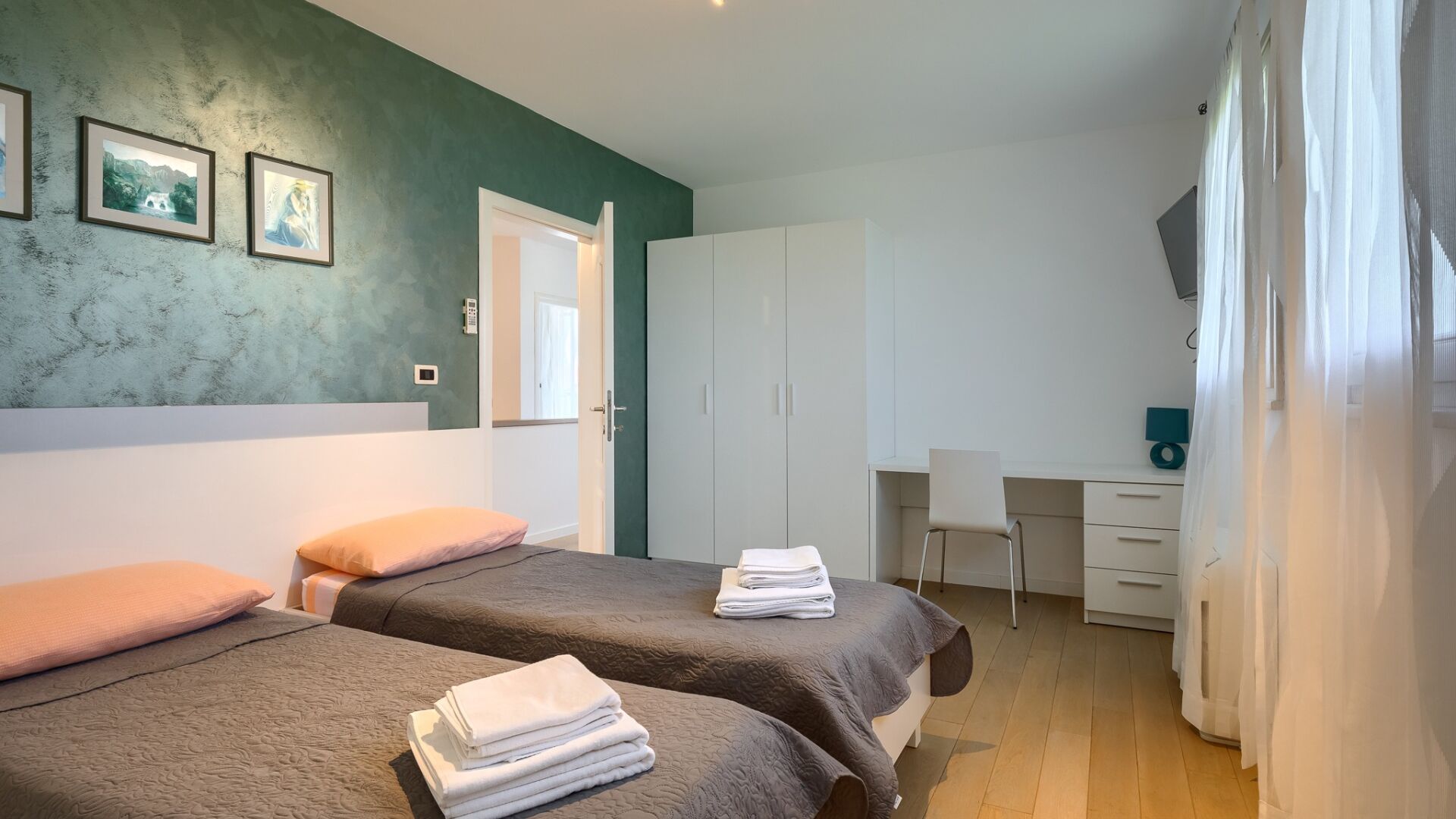 A bedroom with two beds, a desk, and a wardrobe.