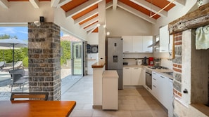 Uma cozinha moderna com armários brancos, um pilar de pedra e uma área de refeições com mesa de madeira.