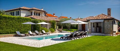 A pool with lounge chairs and umbrellas, a stone patio, and a well-maintained lawn.