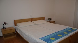 A single bed with a wooden headboard, a bedside table with a lamp, and a small plant on the nightstand.