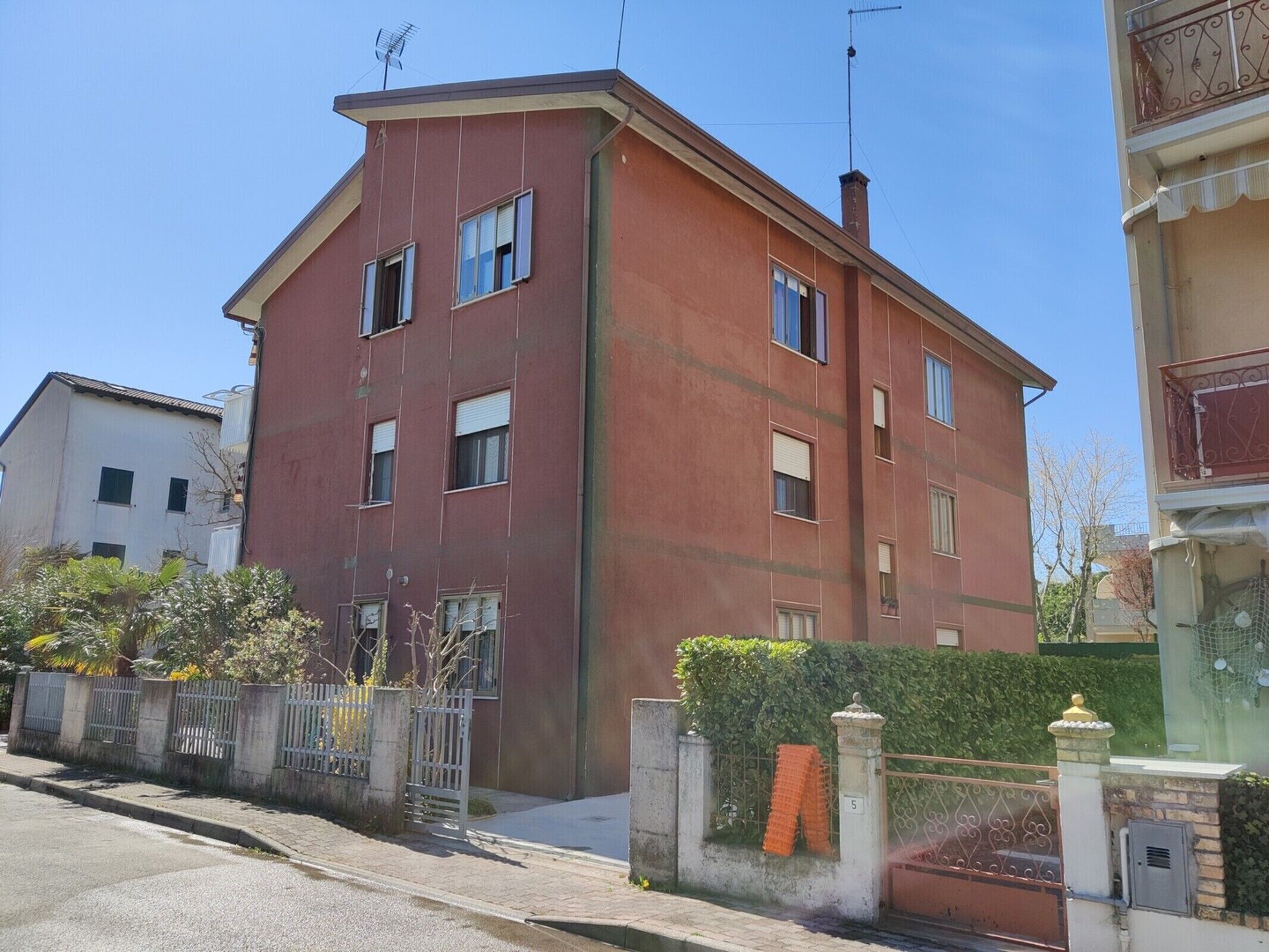 A red two-story building with multiple windows, a gated entrance, and a small garden area.