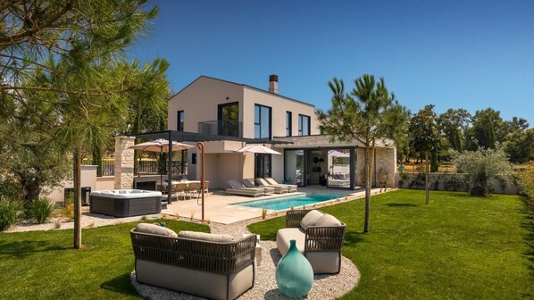 Una casa moderna con piscina, mobiliario exterior y porche cubierto.