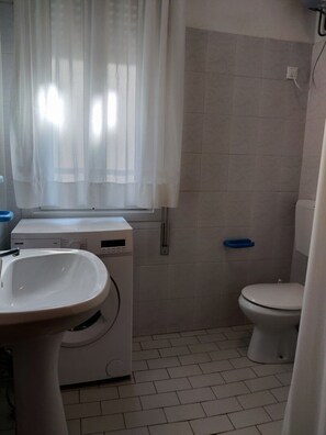Ein kleines, sauberes Badezimmer mit Waschbecken, Toilette und Waschmaschine.