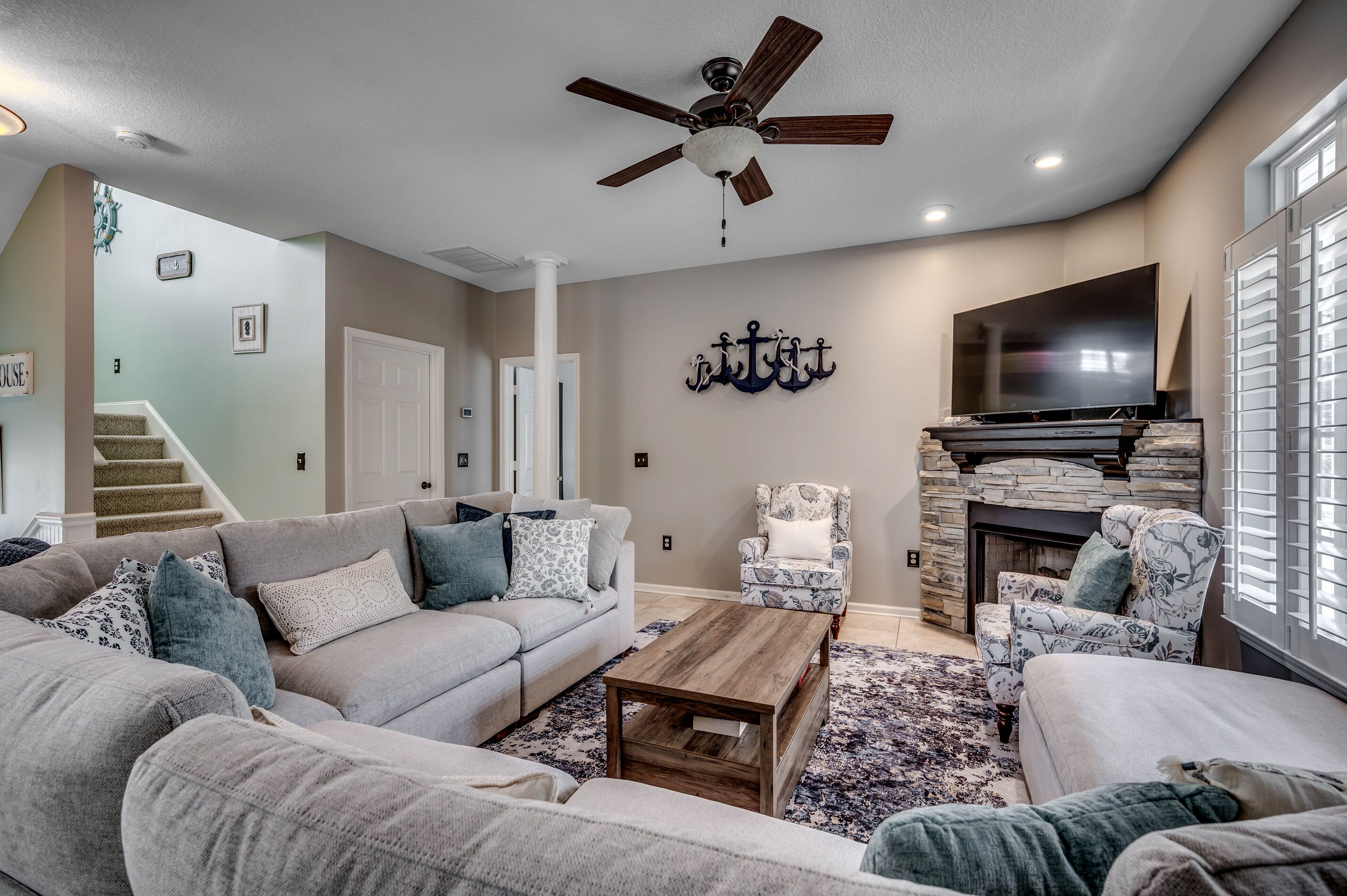 A living room with a sectional sofa, a coffee table, a fireplace, a TV, and a ceiling fan.