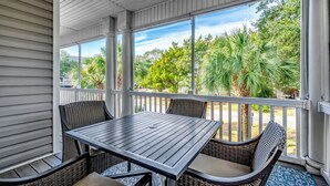 A covered patio with a table and chairs, large windows, and a view of greenery. - Shore Nuff: Surfside Beach. 1 blk to Beach, Private Pool, Golf Cart (Surfside Beach)