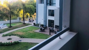 A high-rise building with multiple balconies, a courtyard with outdoor seating, and a view of trees and greenery. - Premier Lifestyle at The Regency (Pretoria)