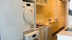 A compact kitchen with a washing machine, a dishwasher, and a refrigerator. - Premier Lifestyle at The Regency (Pretoria)