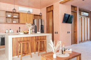 A modern kitchen with wooden cabinets, a stainless steel refrigerator, and a bar area with stools.