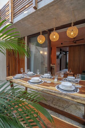 A dining area with a long wooden table set for a meal, featuring a ceiling fan and hanging wicker lamps.