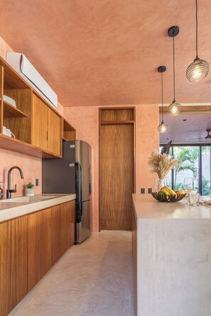 Una cocina moderna con armarios de madera, refrigerador integrado, iluminación colgante y vistas al exterior a través de una ventana.