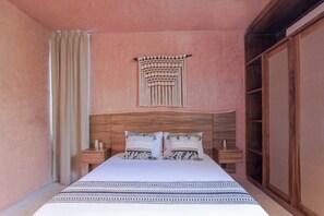 A bedroom with a bed, two nightstands, a wall hanging, and a large window.