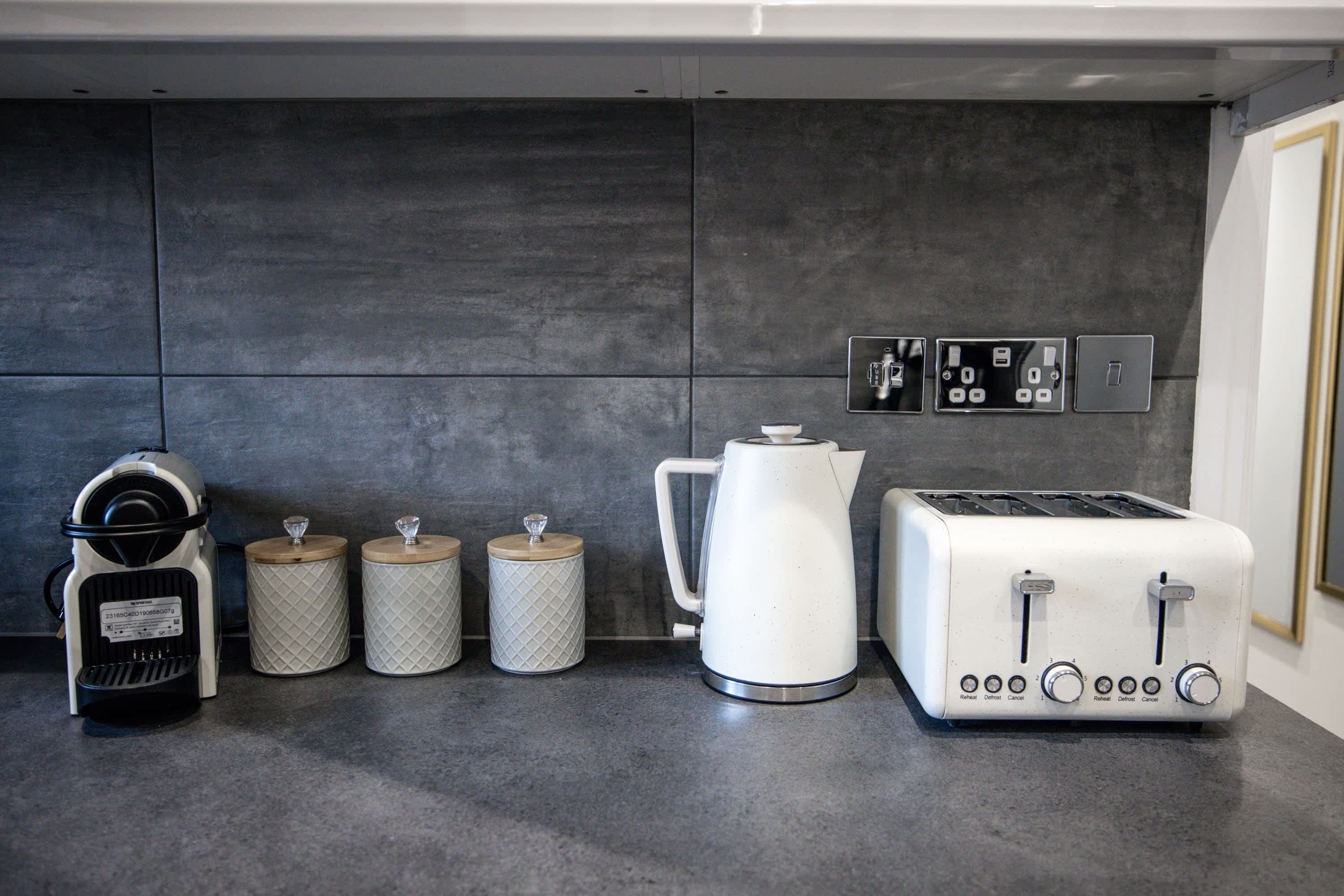 Eine moderne Küche mit Kaffeemaschine, zwei Behältern, einem Wasserkocher und einem Toaster.
