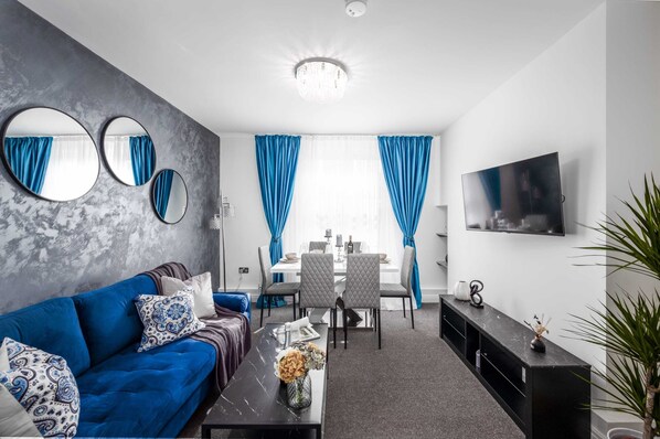Ein modernes Wohnzimmer mit einem blauen Sofa, einem Essbereich mit Tisch und Stühlen sowie einem an der Wand befestigten Fernseher.