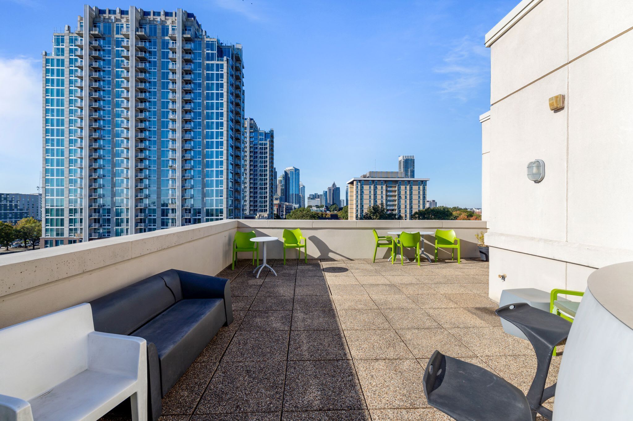 A rooftop terrace with outdoor seating, a view of high-rise buildings, and a clear sky.