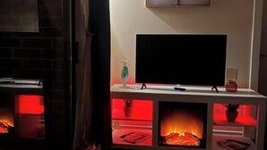 Een woonkamer met een open haard, een televisie op een meubel en een lijst met een afbeelding aan de muur.