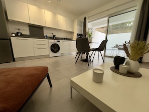 A modern kitchen with a washing machine, dining area with chairs, and a large window.