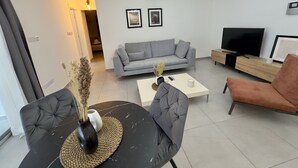 Een moderne woonkamer met een grijze bank, een zwarte salontafel, een televisie en een kroonluchter.