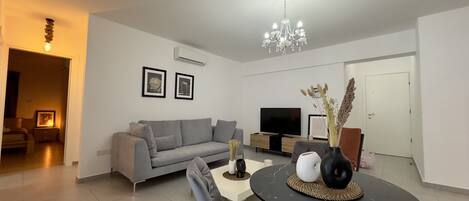 Una sala de estar moderna con un sofá gris, una mesa de centro negra, un televisor y una araña.