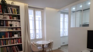 A modern living room with a wooden floor, a round table with two chairs, a bookshelf filled with books, and a television on a stand. - Appartement Montparnasse - rue de la Gaieté (Paris)