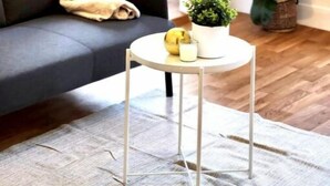 A living room with a grey sofa, a round white table with a plant and a glass, and a large green plant beside the sofa. - Appartement Montparnasse - rue de la Gaieté (Paris)