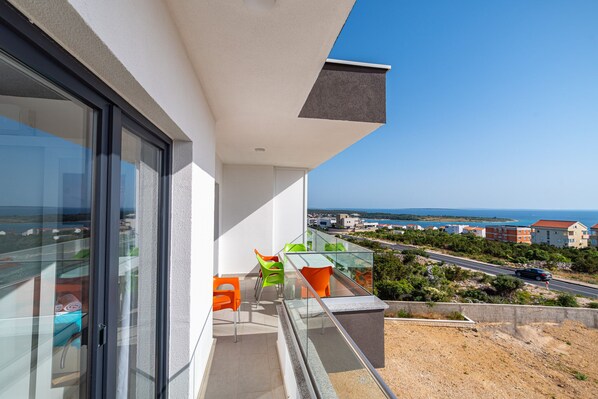 A balcony with a glass door, a small table with chairs, and a view of the coastline.