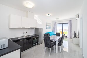 Een moderne keuken met witte kastjes, een zwart aanrechtblad en een eethoek met een tafel en stoelen.