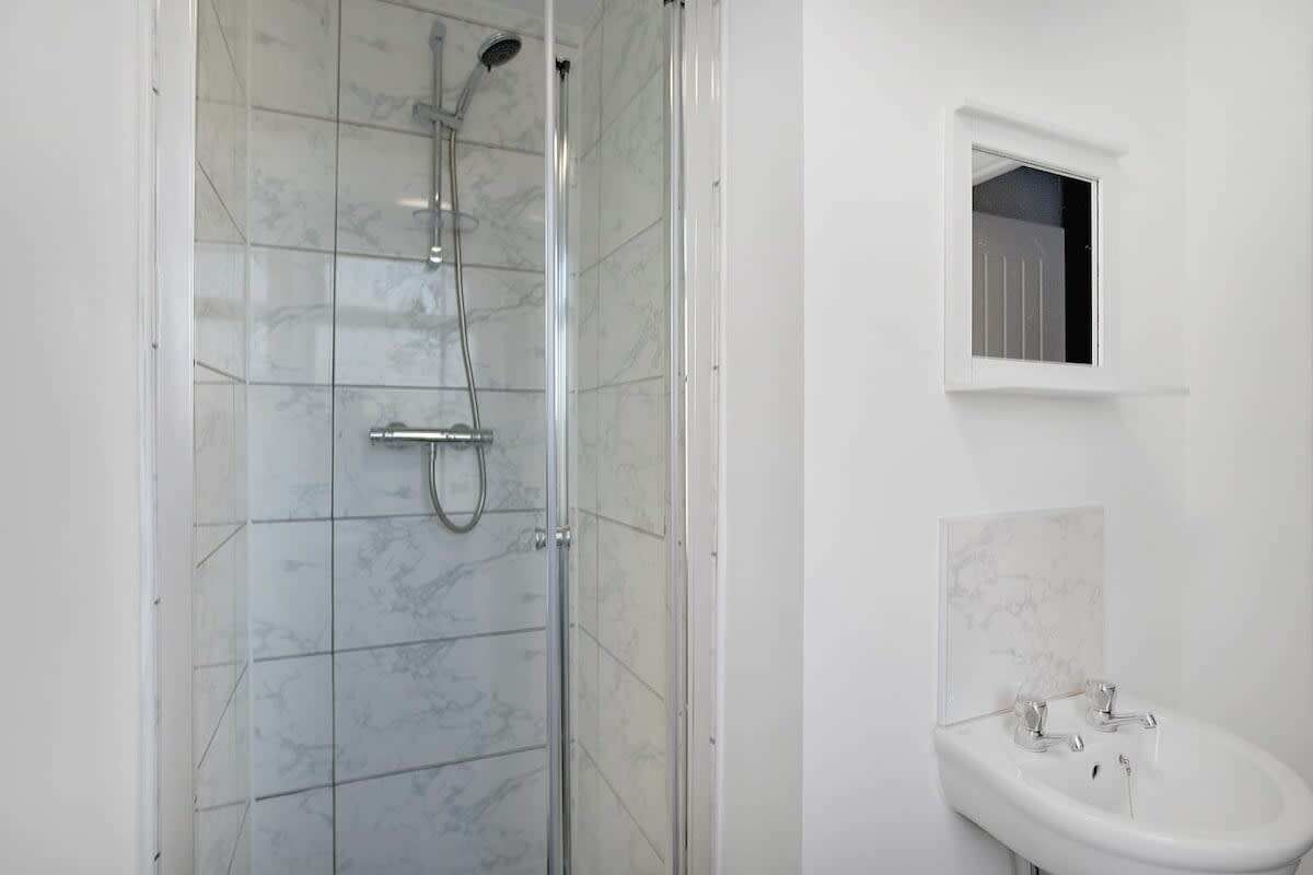 A bathroom with a glass-enclosed shower, a pedestal sink, and a small window.