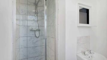A bathroom with a glass-enclosed shower, a pedestal sink, and a small window.