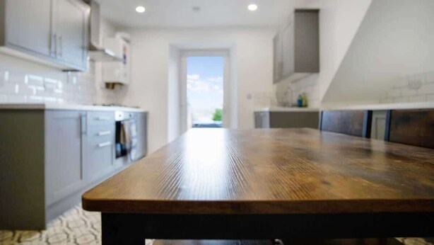 A modern kitchen with a wooden table, grey cabinets, and a view through the doorway.