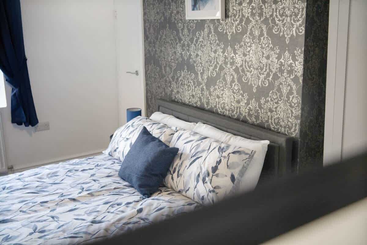 Una cama con una colcha estampada de flores, una única almohada azul y un cabecero frente a una pared con diseño.