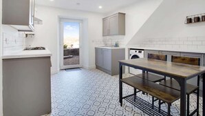 A modern kitchen with a dining area, white cabinetry, and a view through the door.