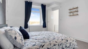 A bedroom with a bed, a window with curtains, a radiator, and a wall-mounted shelf.