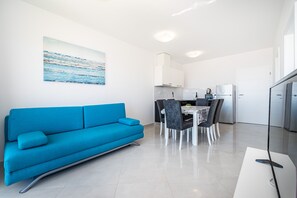 A modern living room with a blue sofa, a dining area with a table and chairs, a kitchen with white cabinets, and a large painting on the wall. - Deluxe Villa Laura 6a (Novalja)