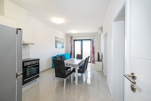 Uma cozinha moderna com forno embutido, uma mesa de jantar com cadeiras e vista para a sala de estar por uma porta de vidro.