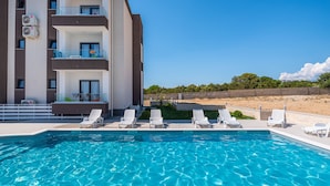 A swimming pool with lounge chairs, a building with balconies, and a clear blue sky. - Deluxe Villa Laura 0a (Novalja)