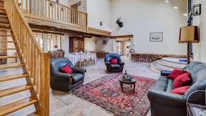 Ein geräumiger Wohnbereich mit einer Holztreppe, Ledersofas, einem gemusterten Teppich und einem Essbereich im Hintergrund.