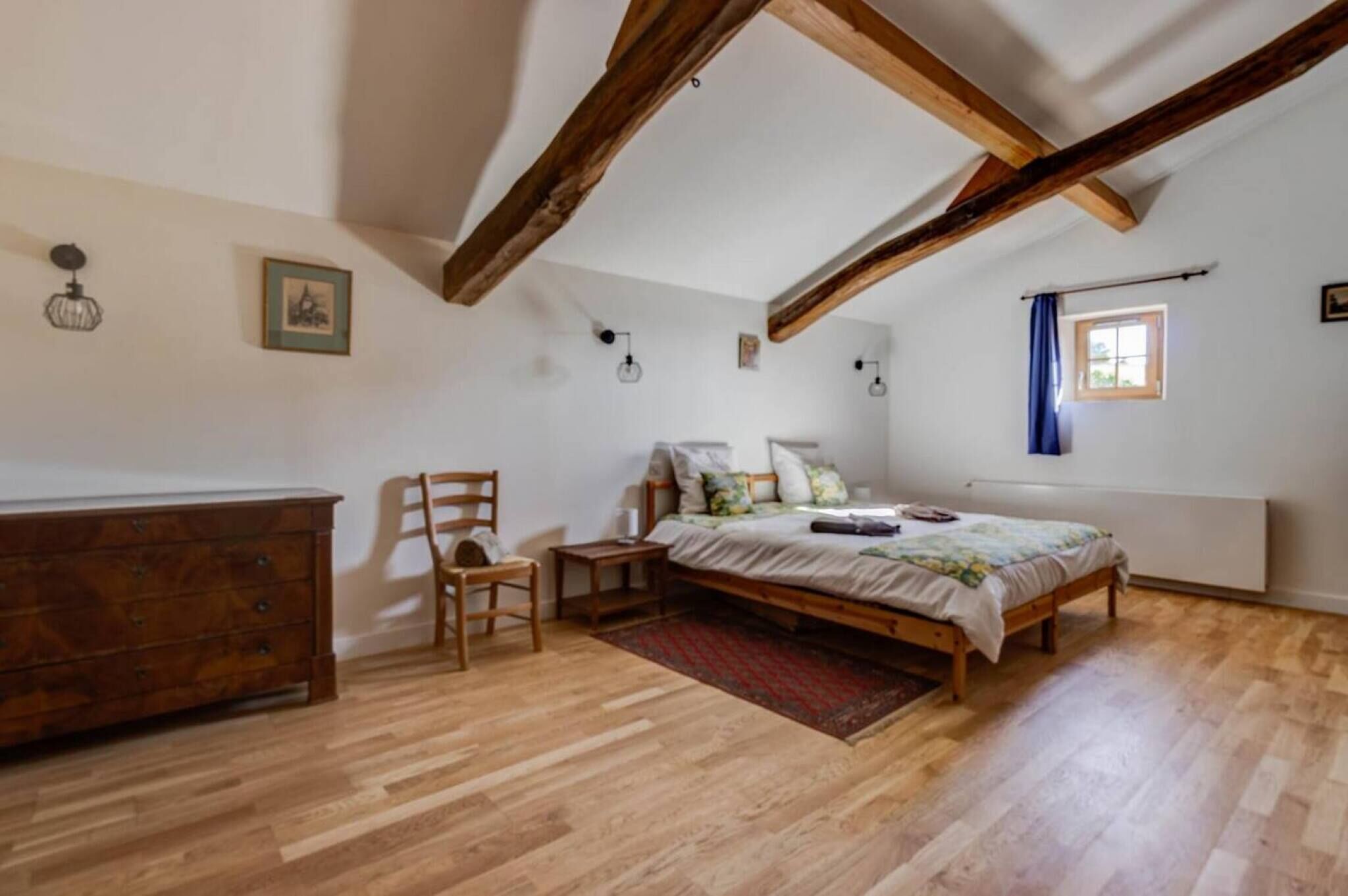 Een slaapkamer met een houten bed, een dressoir, een stoel en een klein tafeltje.
