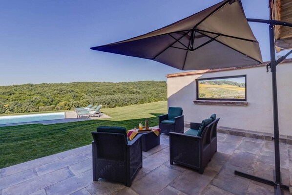 An outdoor patio with wicker furniture, a large umbrella, and a view of a pool and green landscape. - Getaway at La Métairie de Rouzies - Swimming pool (Tauriac)