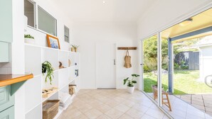 A bright, spacious room with a large sliding glass door leading to a garden. There are white shelves with various items, including plants and a wooden bench.