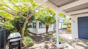 A covered patio area with a barbecue grill, potted plants, and a small seating area. - Evoke - Shoal Bay, 2 Leonard Ave , Stylish holiday house with air con, Wi-Fi & boat parking (Shoal Bay)