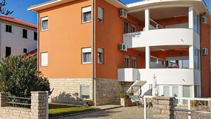 Ein zweistöckiges Gebäude mit flachem Dach, einem Balkon im oberen Stockwerk und einer kleinen Terrasse mit Grill.