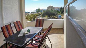 Ein Balkon mit Tisch und Stühlen, Blick auf eine Straße und Gebäude, und ein geparktes Auto davor.